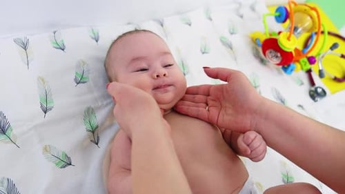 Pediatrician touching and feeling baby’s neck. Little beautiful child lies peacefully during doctor’