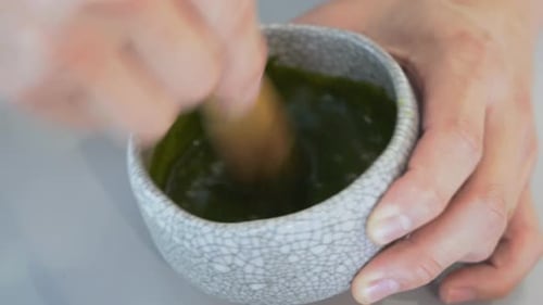 Handheld close up shot of a pair of hands whisking and mixing match green tea in the handmade cerami