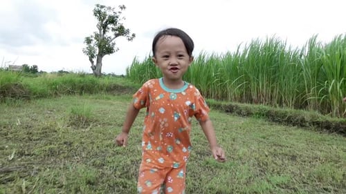 A boy enjoys running outdoors amidst vibrant green grass under a cloudy sky