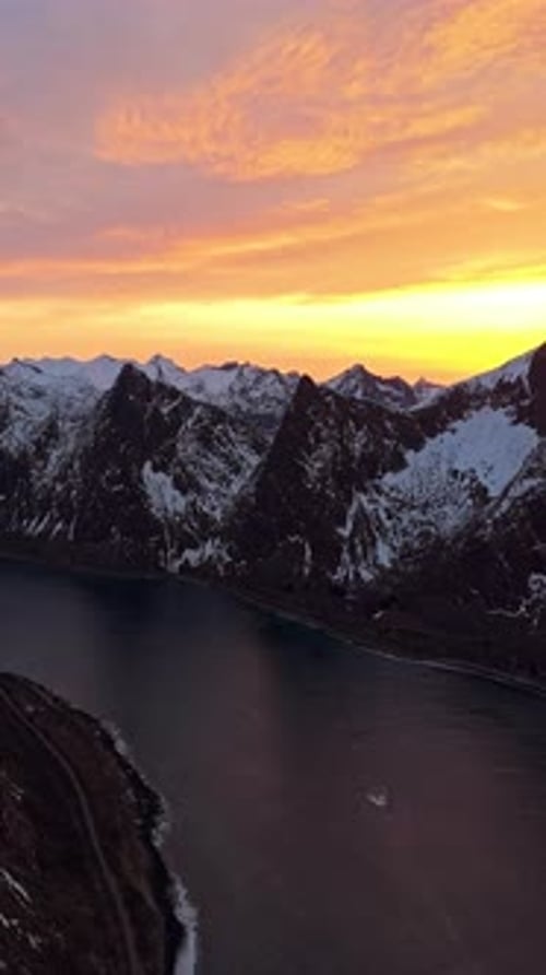 Coucher de soleil vibrant illuminant les sommets enneigés et les eaux sombres du fjord
