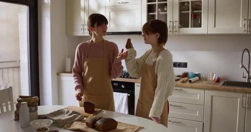 Woman in Apron Cutting Piece of Bread and Giving It to Her Daughter to Try After Baking Homemade