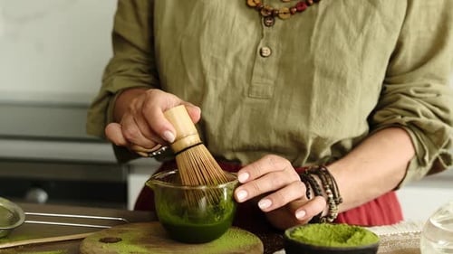 Woman Preparing Matcha Tea with Bamboo Whisk in Kitchen