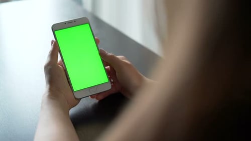 Young woman browsing social media on smartphone with green screen indoors