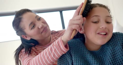 Woman Brushes Smiling Girl's Curly Brown Hair