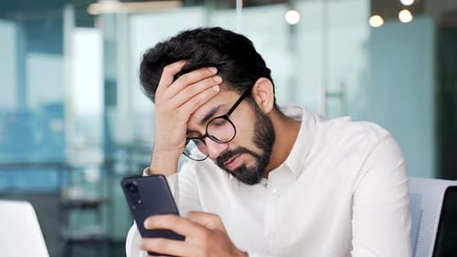 Close up. Frustrated stressed young businessman reads bad news on a smartphone while sitting at work