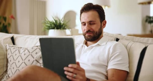 Man Relaxing on Couch Using Tablet and Smiling