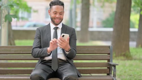 Excited Businessman Celebrating Success on Smartphone in Park