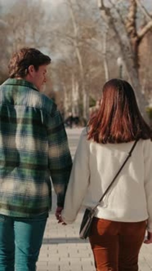 Happy young couple man and woman walking holding hands on the street, back view