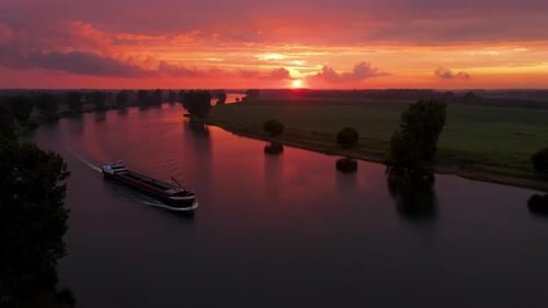 An aerial shot of a Beautiful sunset over Dutch river with a vessel passing by in an orange and red