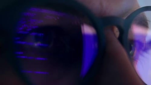 Augen eines erwachsenen Mannes mit Brille, der am Programmcode arbeitet und auf den Computerbildschirm schaut