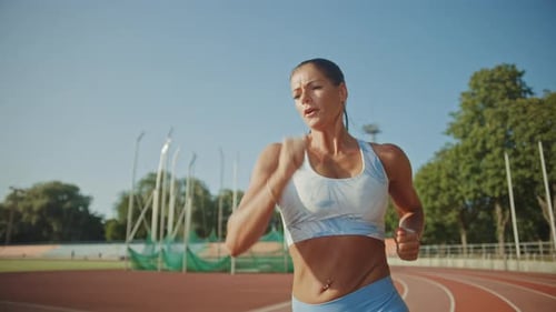 Close Up Portrait Shot of a Beautiful Fitness Woman in Light Blue Athletic Top Jogging in a Stadium