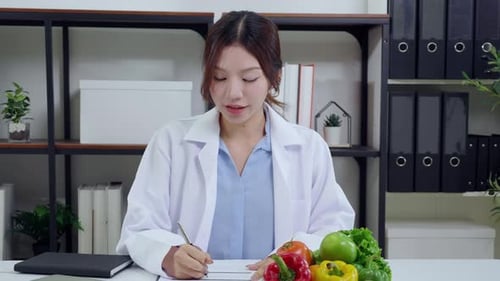 Asian nutritionist using laptop in clinic office, online consultation, healthcare advice.
