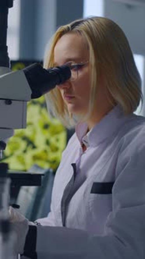 Woman Scientist Uses Microscope and Writes Notes in Lab