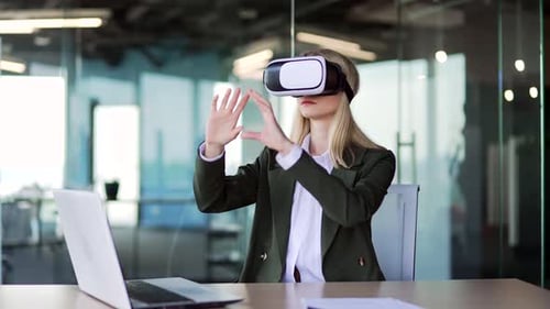 Young successful businesswoman works using VR glasses in virtual reality simulator while sitting