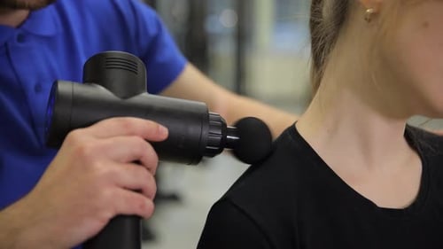 Professional Masseur Using Percussion Massage Gun on Woman's Neck