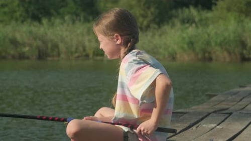 Kleines Mädchen fischt morgens alleine am Fluss mit Angelrute