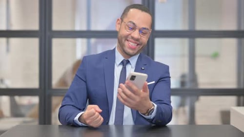 Mixed Race Businessman Celebrating Success on Phone in Office