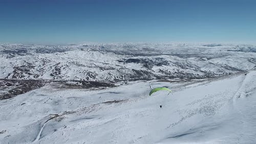 Luftaufnahme eines Mannes beim Gleitschirmfliegen auf einem Berg im Winter