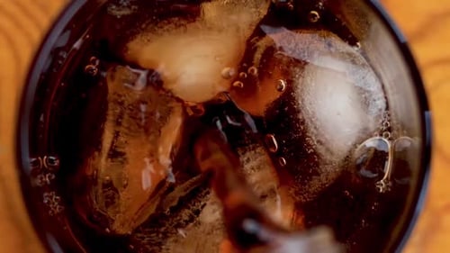 Pouring dark liquid over ice in glass