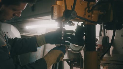 Um trabalhador trabalha em uma furadeira de metal em uma oficina