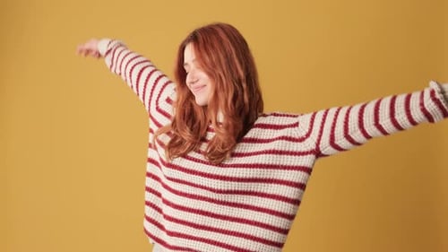 Happy girl dancing in studio on yellow background