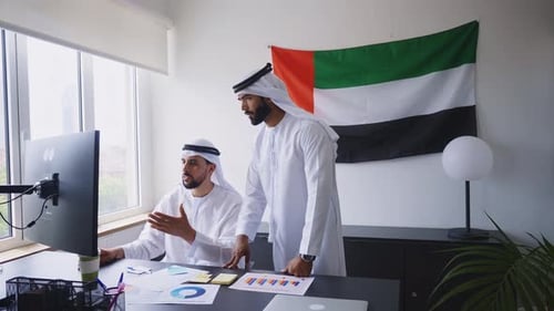 two businessmen working together in a modern office in the united arab emirates.