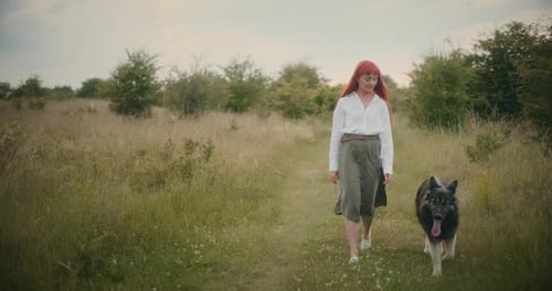 Woman and Dog Walk Through a Grassy Field