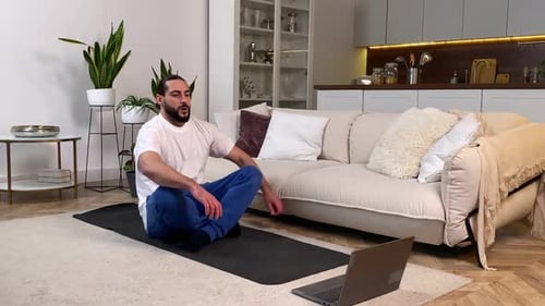 Hombre meditando siguiendo clases de yoga en línea a través de una computadora en el interior
