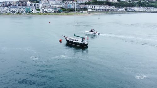 Power boat aerial dolly left view navigating Conwy marina around sailboat with mast at seaside town