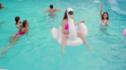 Pretty Woman in Bikini Swimsuit Hanging Out on Inflatable White Swan Mattress on Night Pool Party
