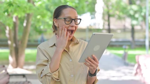 Woman Celebrates Success on Tablet in City Park