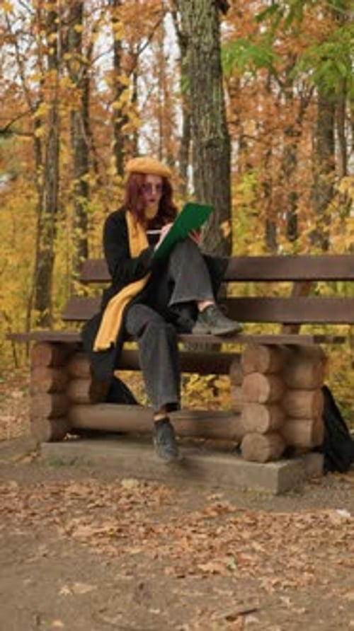 Female Artist Sketching on Wooden Park Bench Surrounded By Autumn Foliage