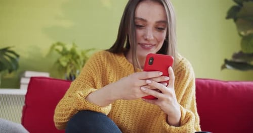 Smiling woman using phone sitting on red couch