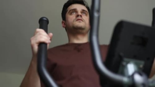 middle age man doing exercises on elliptical trainer in living room at home