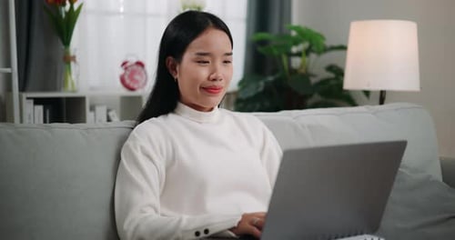 Woman Using Laptop on Gray Couch Indoors