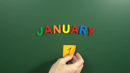 Hand sticking a sticker 1 January calendar day on school board. 1 date of January. First day