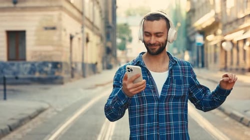 A Young Traveler Wearing Stylish Headphones Happily Strolls Through the Old City Center Listening to