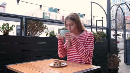 young woman sitting at a street cafe table, sipping coffee and eating dessert