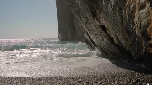 Powerful Waves Crash Against the Cliff, Sending Mist into the Air as the Sunlight Glimmers on the