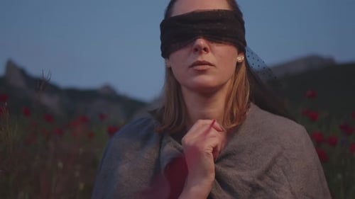 A Woman with a Black Blindfold Among a Field of Poppies Against the Backdrop of Mountains in the