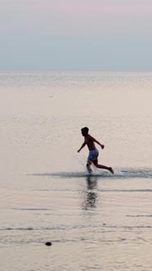 Tourist Running in Shallow Waters on a Tropical Beach at Sunset with a Luxury Yacht in the