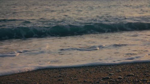Gentle waves washing over pebbles at sunset on Mediterranean beach in soft golden light