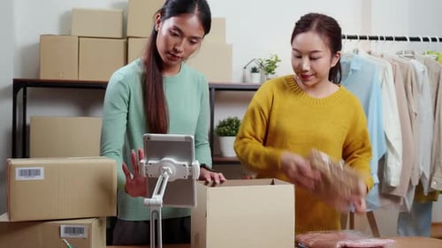 Two young asian woman online seller packing clothing orders in home office.