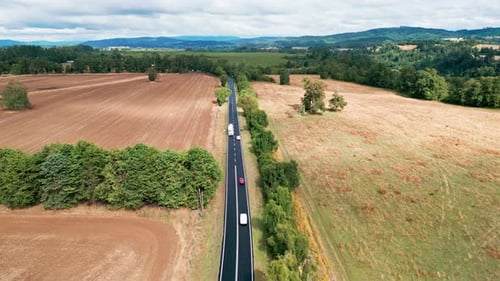 Flyover of straight road with cars through agricultural fields and forest