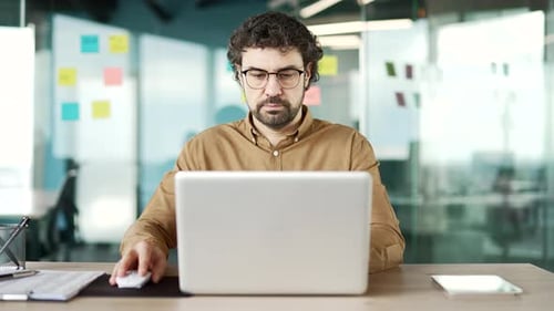 Bearded businessman using a laptop sitting at a desk at workplace in a business office. Entrepreneur