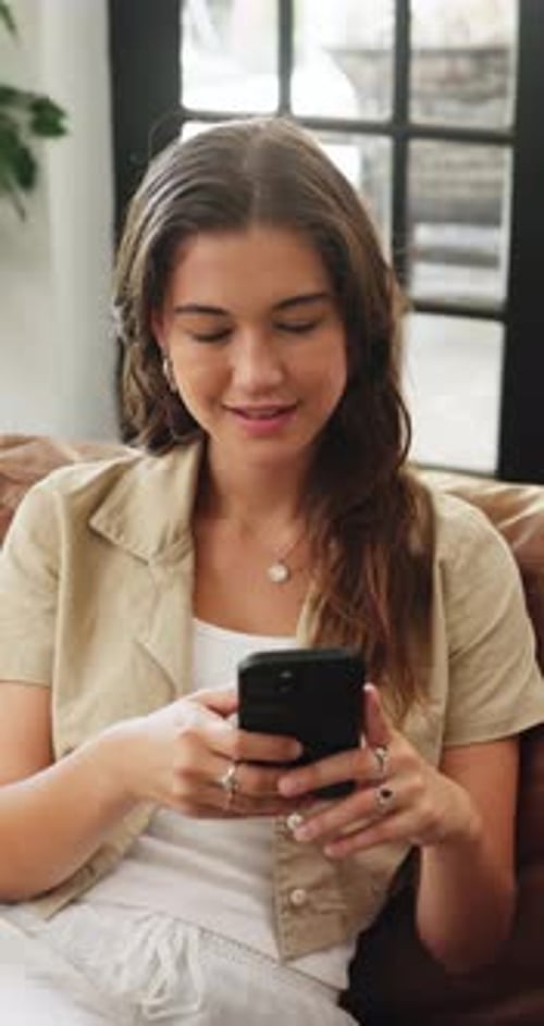 Young Woman Uses Mobile Phone Sitting on Sofa