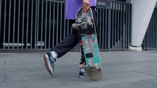 Unknown hipster man walking at city street carrying longboard near stadium