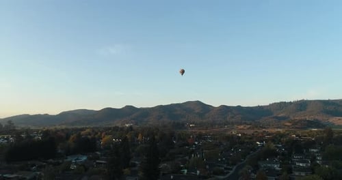 fall back aerial of hot air balloon rising over small town in the Napa Valley