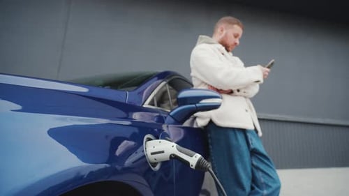 Man Using Smartphone While Charging Electric Car
