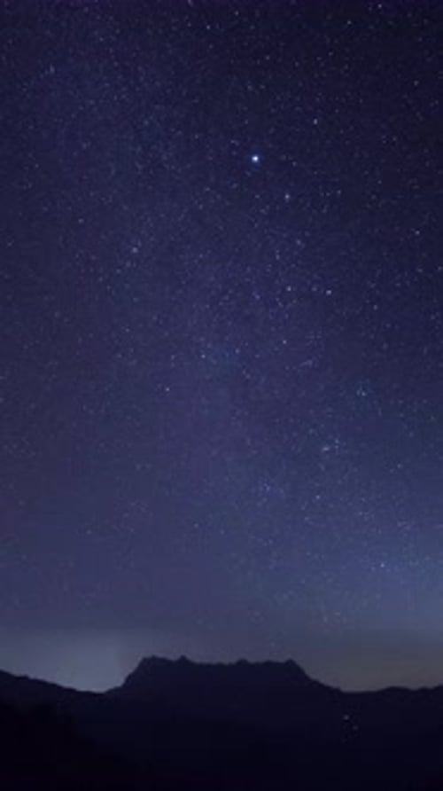 Starry night over mountain vertical time lapse video of stars in dark night sky.